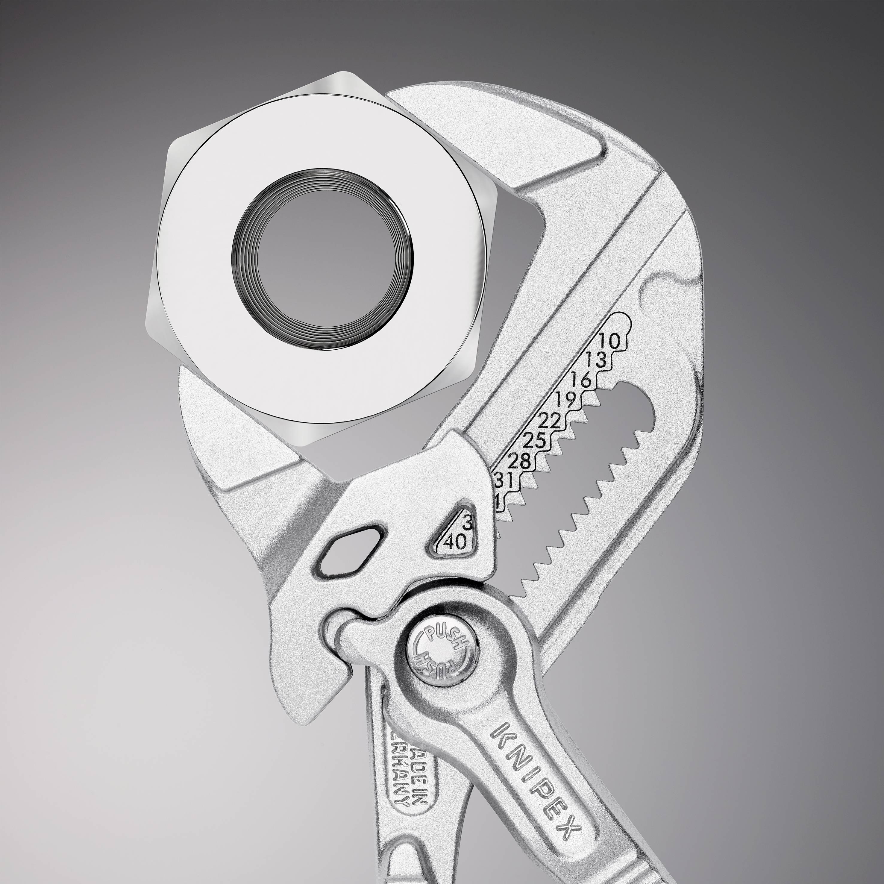 An adjustable spanner grips a large hexagonal nut in focus. The spanner displays metric measurements and is crafted from silver-coloured metal.