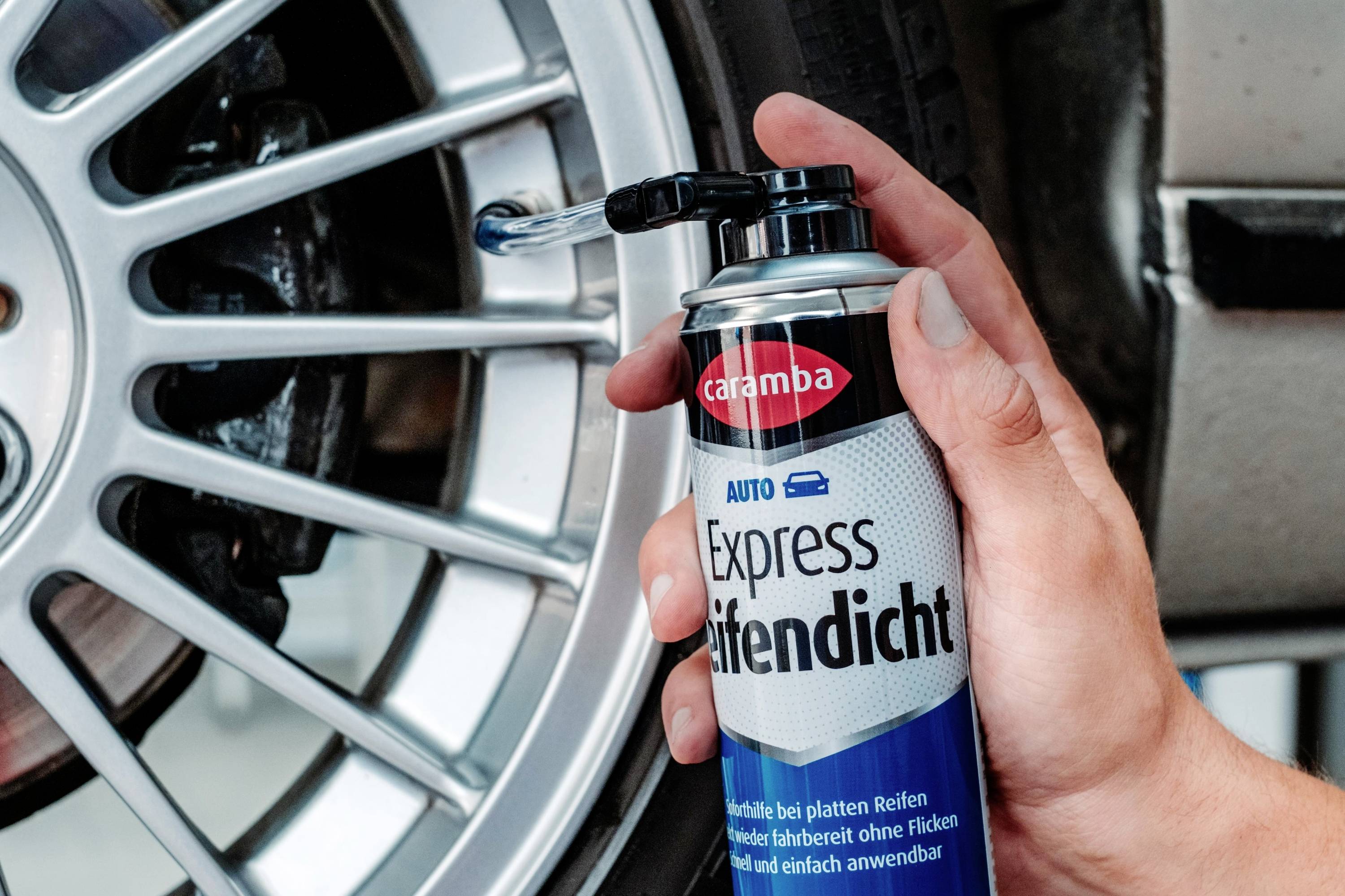 'A hand holds an aerosol can labeled Express Reifendicht, near a car tire rim, suggesting use for tire maintenance or repair.'