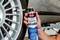 Person using a can of 'Caramba Auto Express Reifendicht' tire sealant to repair a car tire on a vehicle lift in a garage setting.