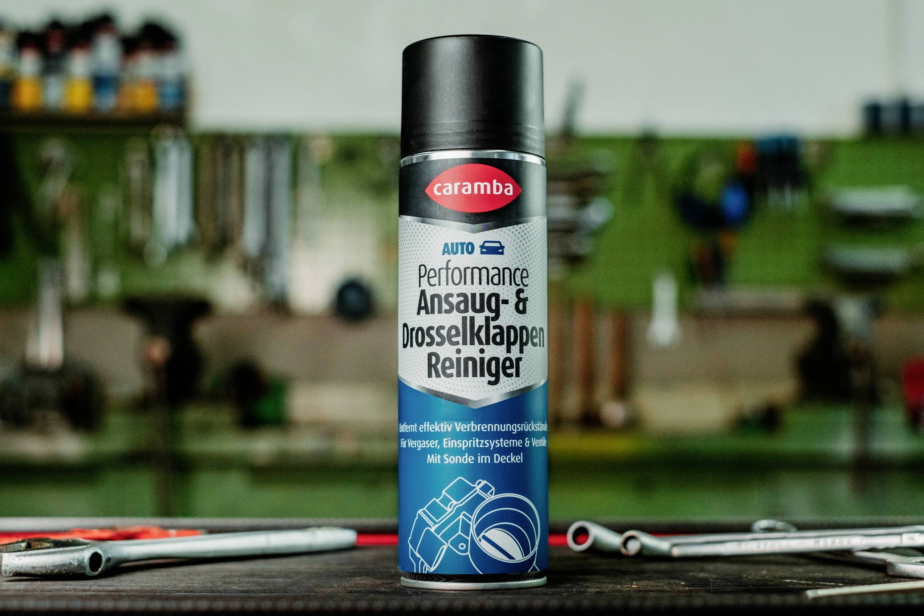 A can of 'Performance Ansaug- & Drosselklappen-Reiniger' by Caramba is placed upright on a workbench with tools nearby in a garage setting.