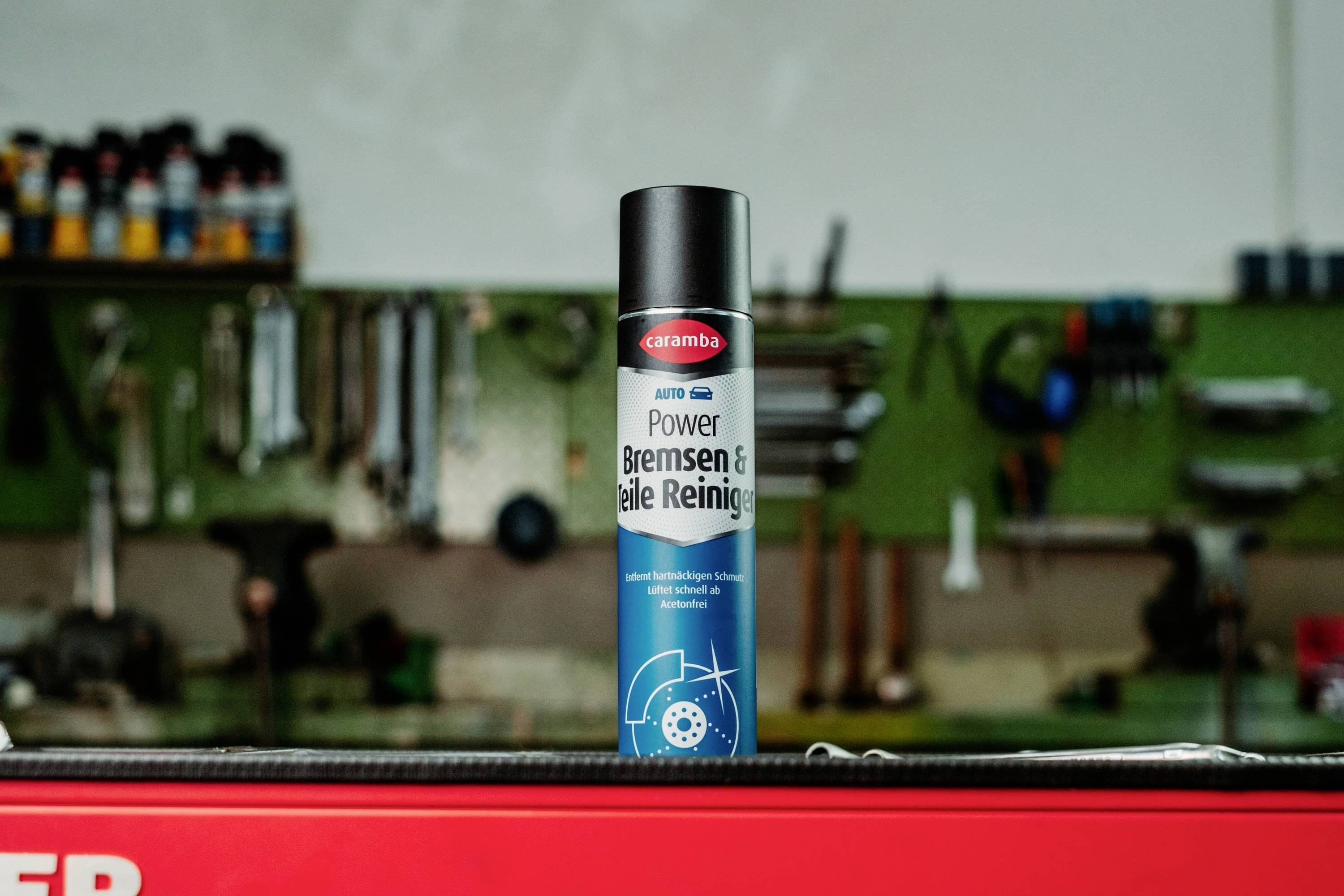 A can of 'Caramba Power Bremsen & Teile Reiniger' brake and parts cleaner stands on a red surface in a workshop with tools in the background.