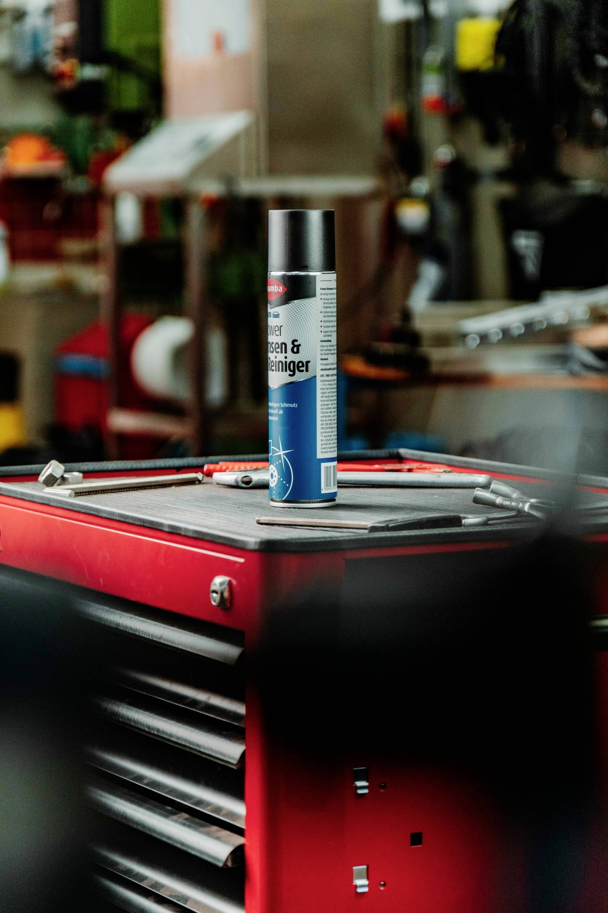 A canister of cleaner stands on top of a red tool chest in a busy workshop. Various tools and equipment are visible in the background.