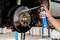 A hand sprays brake cleaner onto a car's brake disc, in a garage setting, illustrating maintenance or repair work on the vehicle.