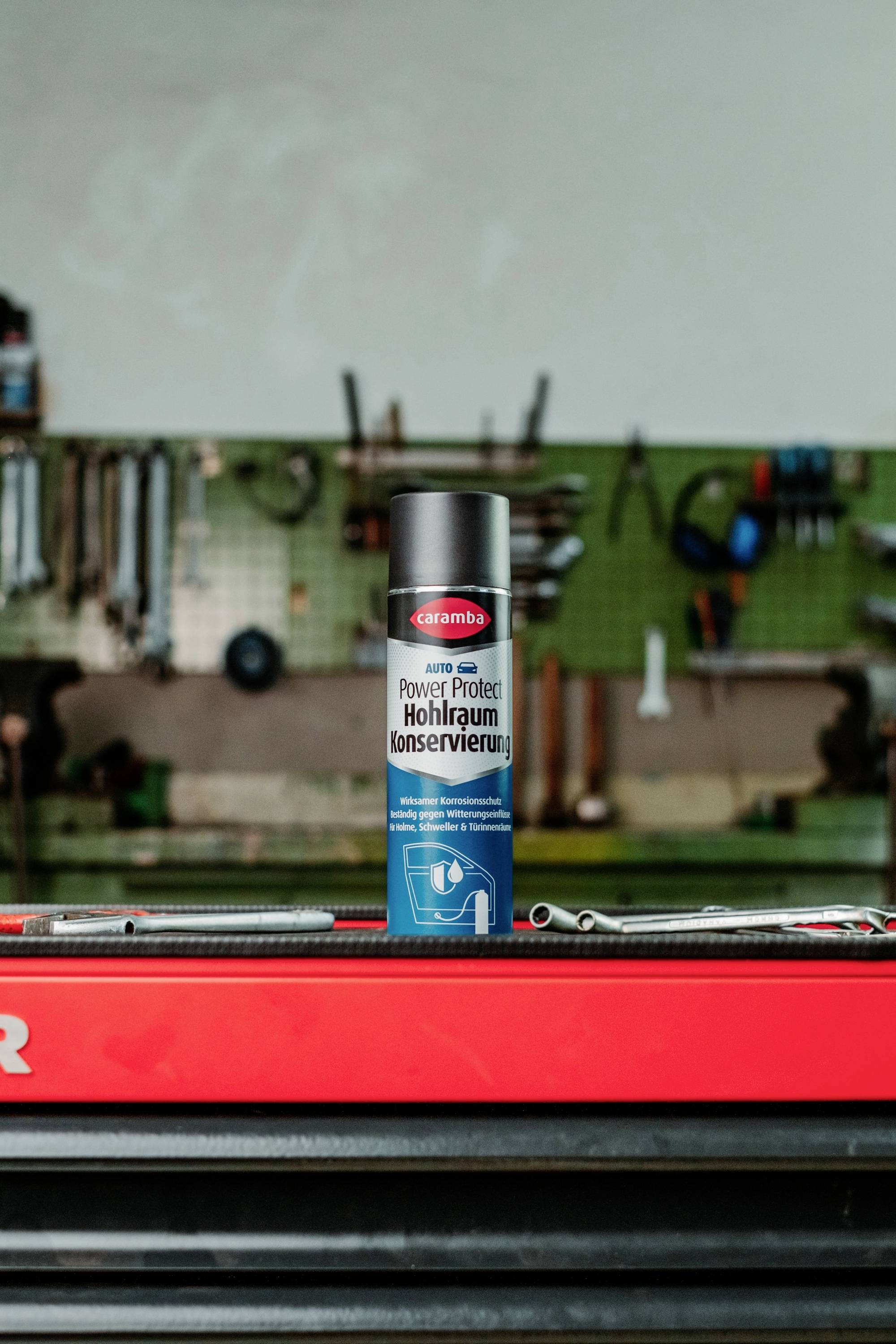 A can of 'Caramba Hohlraumkonservierung' stands on a red tool chest in a workshop, with tools hanging on a pegboard in the background.