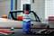 A can of 'Caramba Power Protect Unterbodenschutz' rust protection spray stands on a table with tools, in front of a classic car.