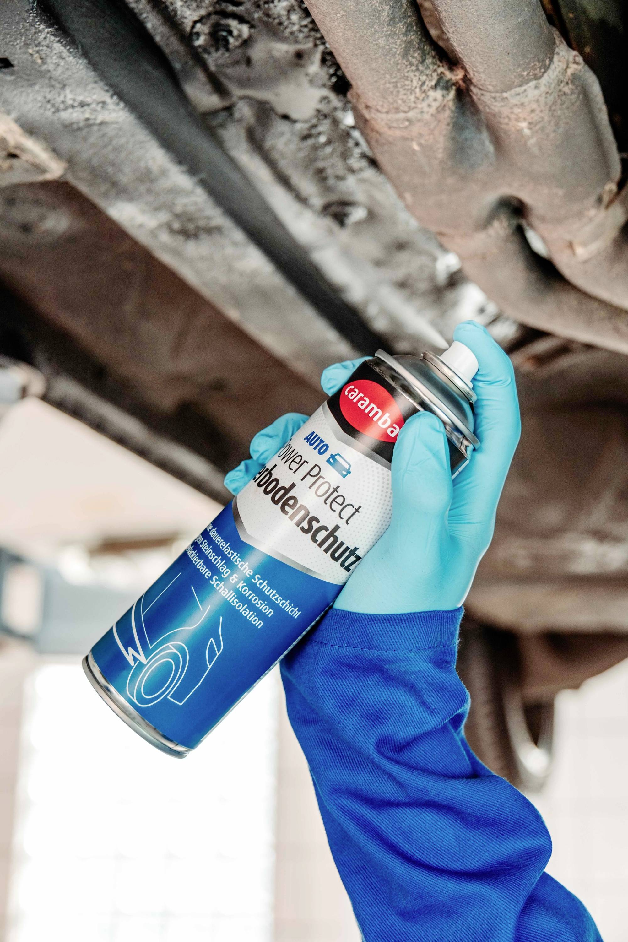 A person wearing gloves sprays undercarriage protection on the underside of a vehicle to prevent rust and corrosion, ensuring durability.