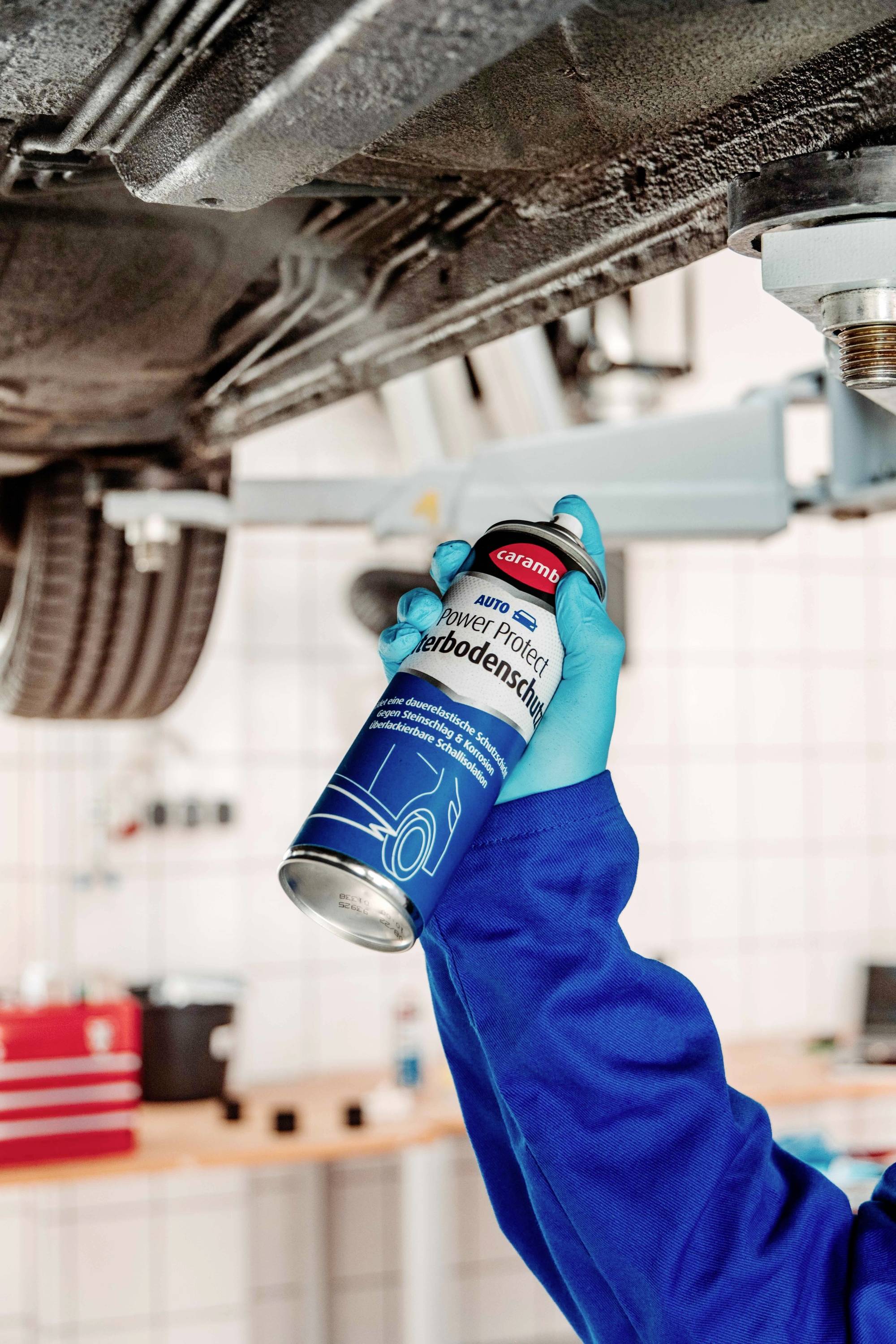 A person in protective gloves sprays undercarriage coating on a car's underside, highlighting vehicle maintenance.