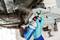 A mechanic in blue gloves applies protective spray to a car's underbody using a can labeled 'Power Protect Bodenschutz'.