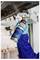 Worker in blue gloves holds a spray can and applies undercoating or rust protection to the underside of a vehicle on a lift.