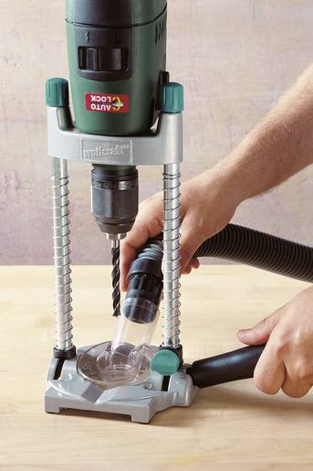 An electric drill is held vertically using a drill stand mount while someone is working on a wooden surface.