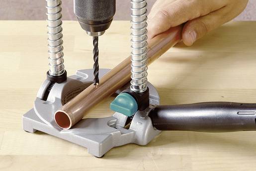 A person is drilling into a wall with a green drill and a hose vacuum attachment. Pictures can be seen in the background.