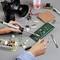 A person is soldering electronic components onto circuit boards. Surrounded by cameras and technical components.