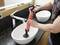 A person is using an orange hand pump in a sink to clean it. Water is flowing into the basin. A second basin is visible in the background.