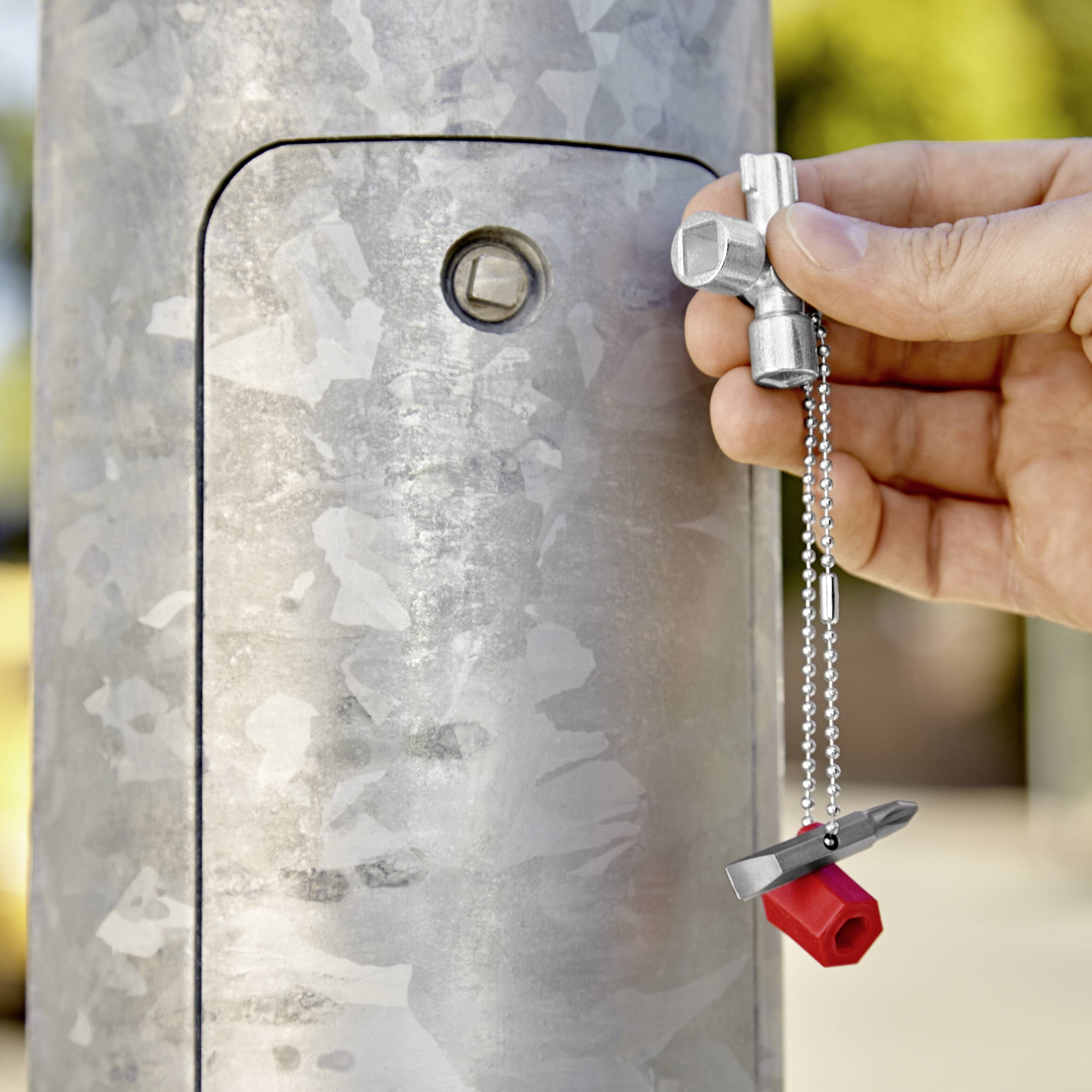 A hand holds a silver key, unlocking a square lock on a grey metal post.