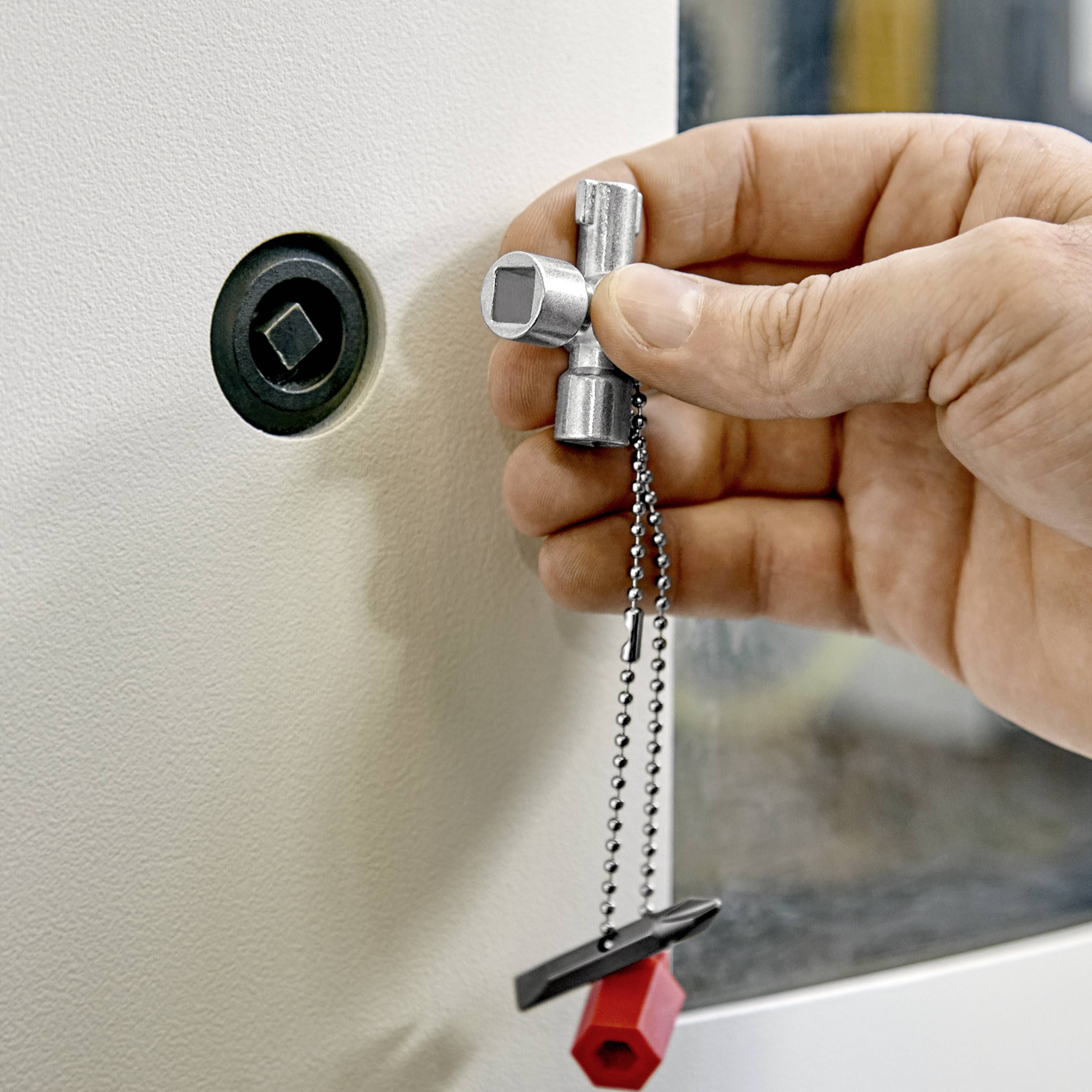 A hand is holding a silver key with a red tag and inserting it into a circular lock on a white door.