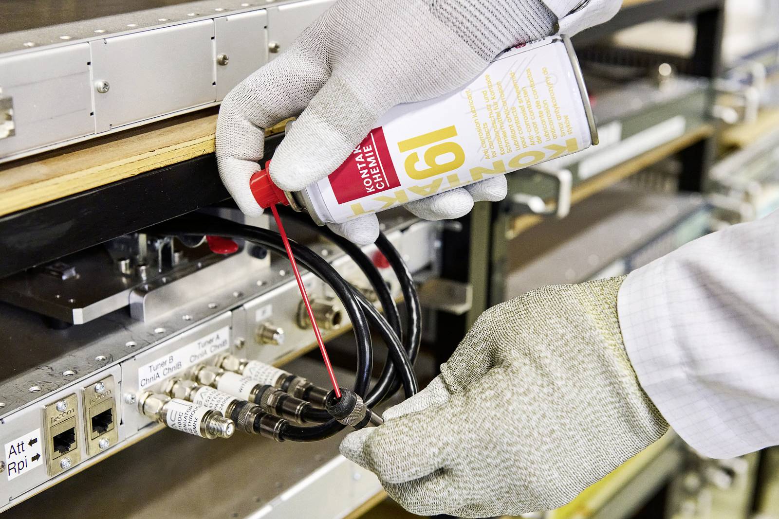 A person wearing gloves is cleaning cable connections on a technical installation with a spray.