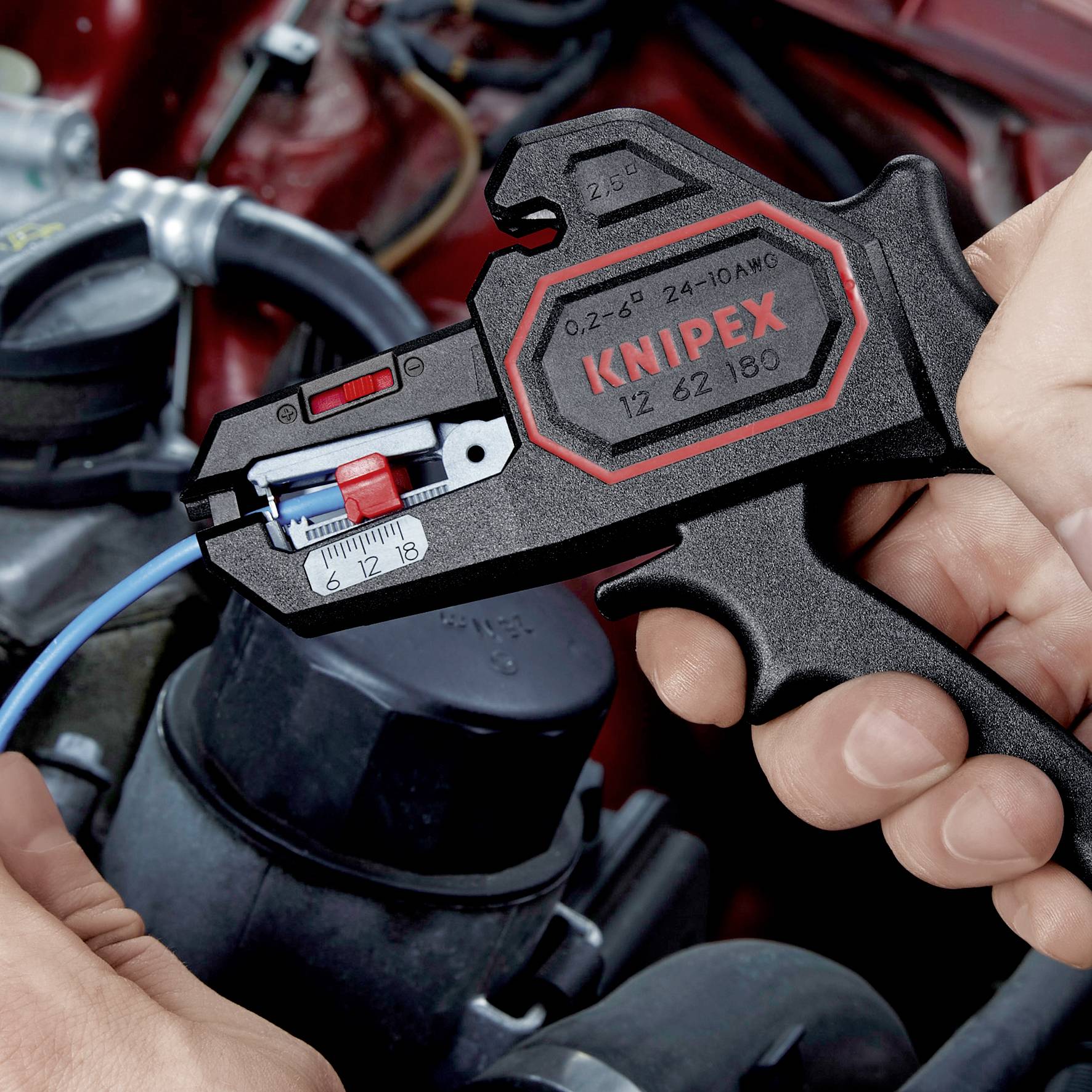 A hand is holding a black and red wire stripping pliers working on a wire. Motor components are visible in the background.