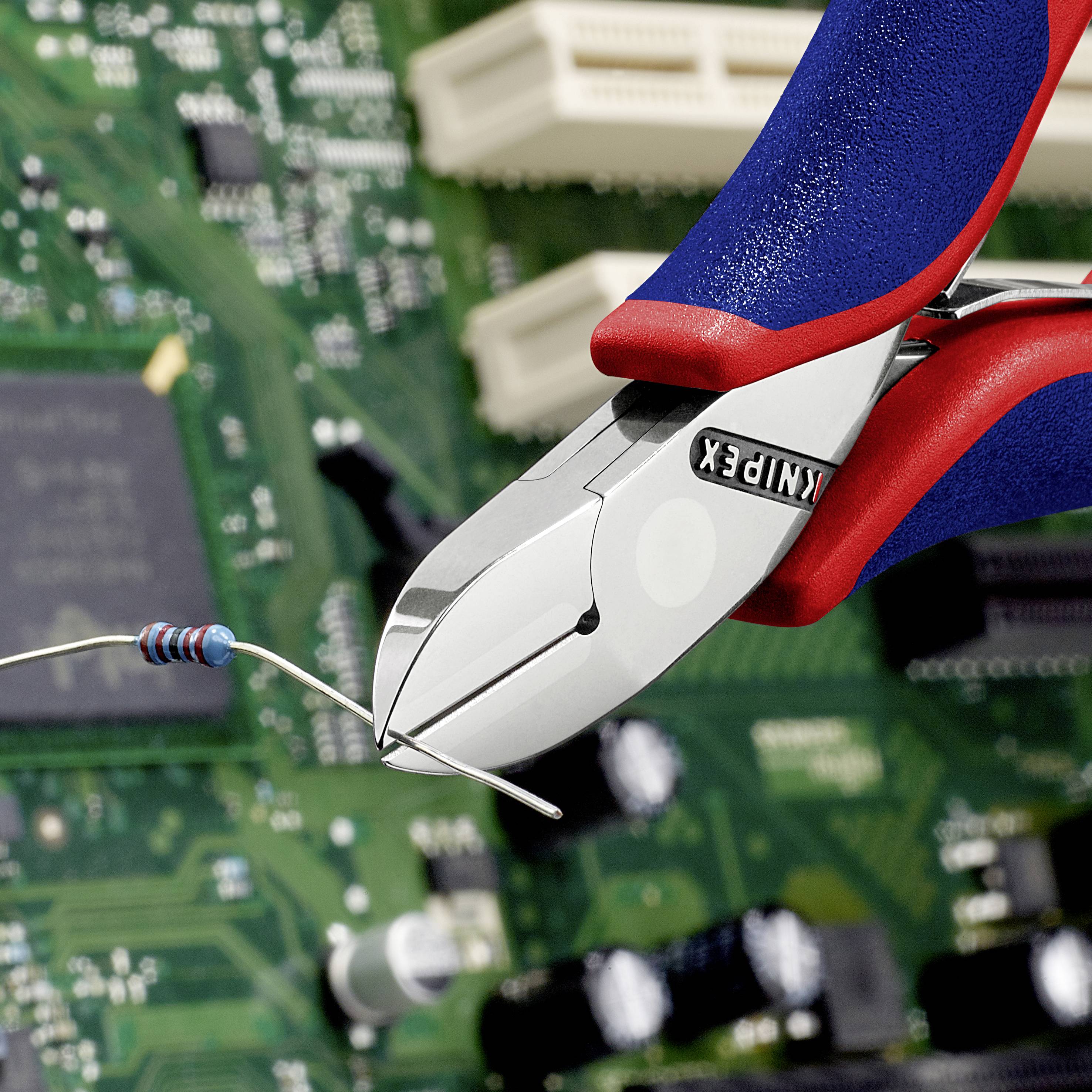 A close-up of an electronic wire being cut with red and blue side cutters in front of a circuit board.