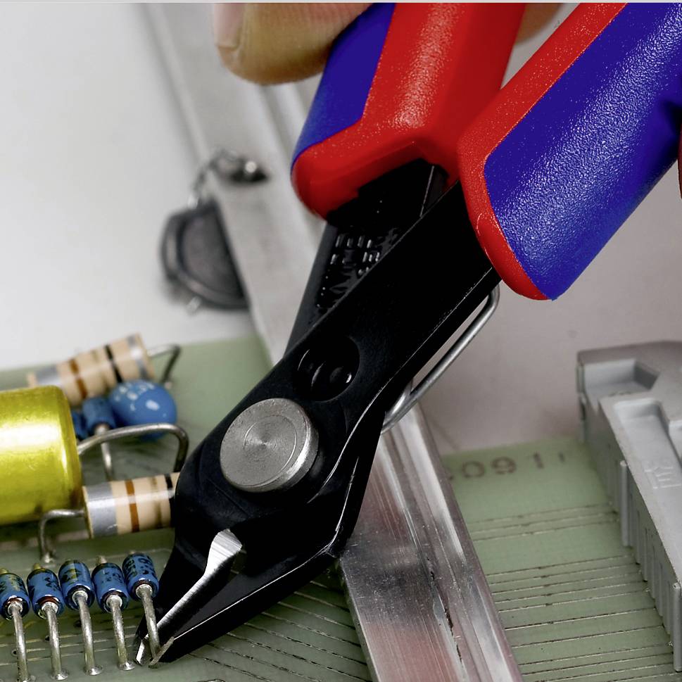 A hand holds pliers cutting an electronic component on a circuit board. Additional components are visible in the background.