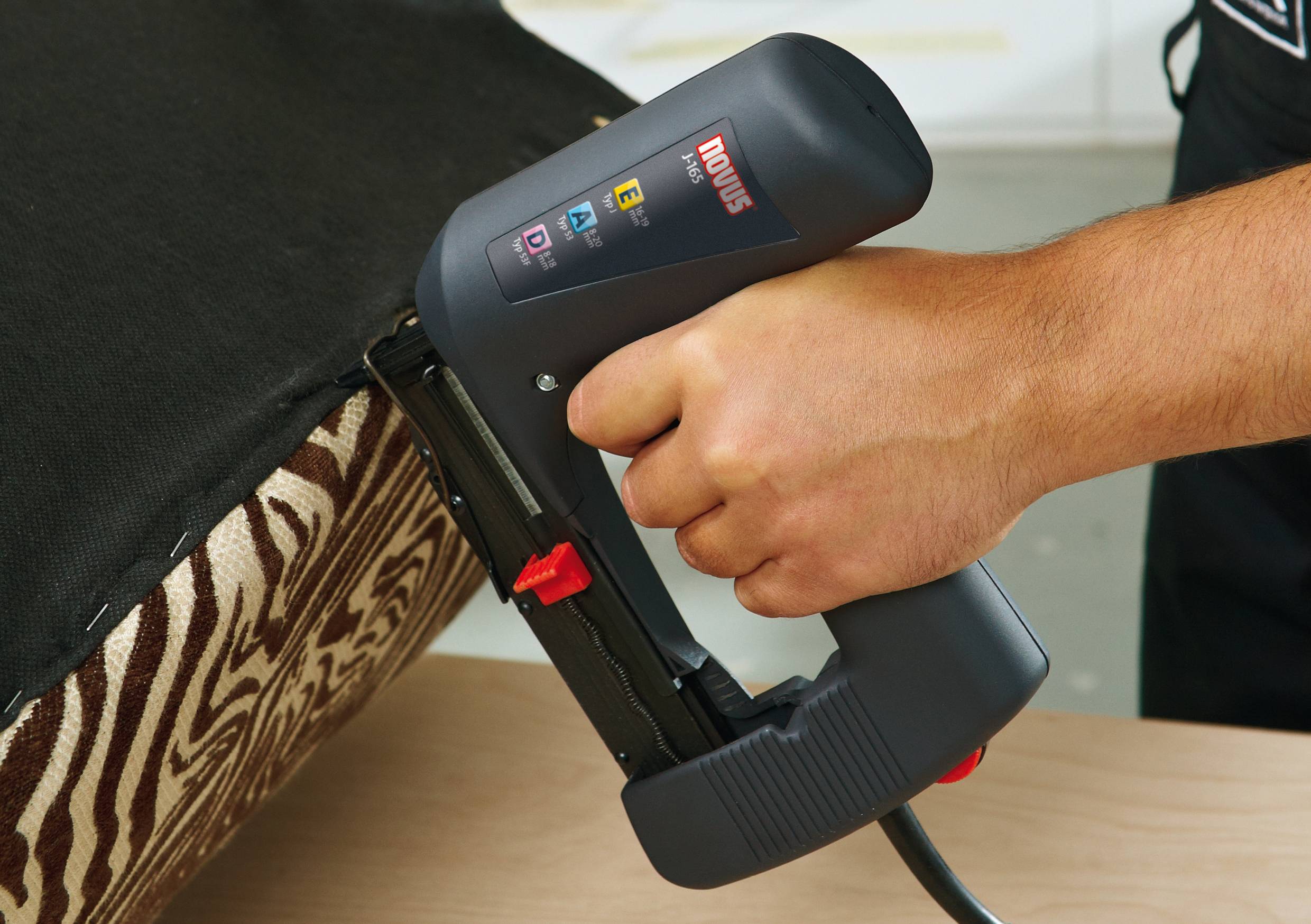 A person is holding an electric staple gun and fixing a black fabric onto a zebra-patterned piece of furniture.