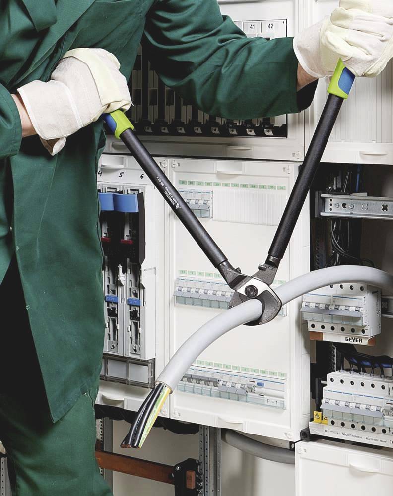 A person wearing green workwear is using pliers to cut a thick cable inside an open electrical cabinet.