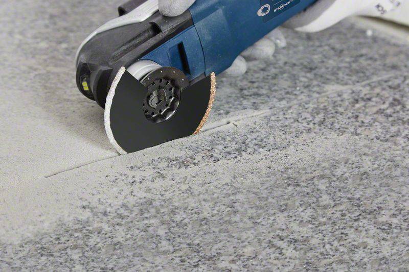 A hand holds an angle grinder, which is being guided over a grey stone surface, generating dust.