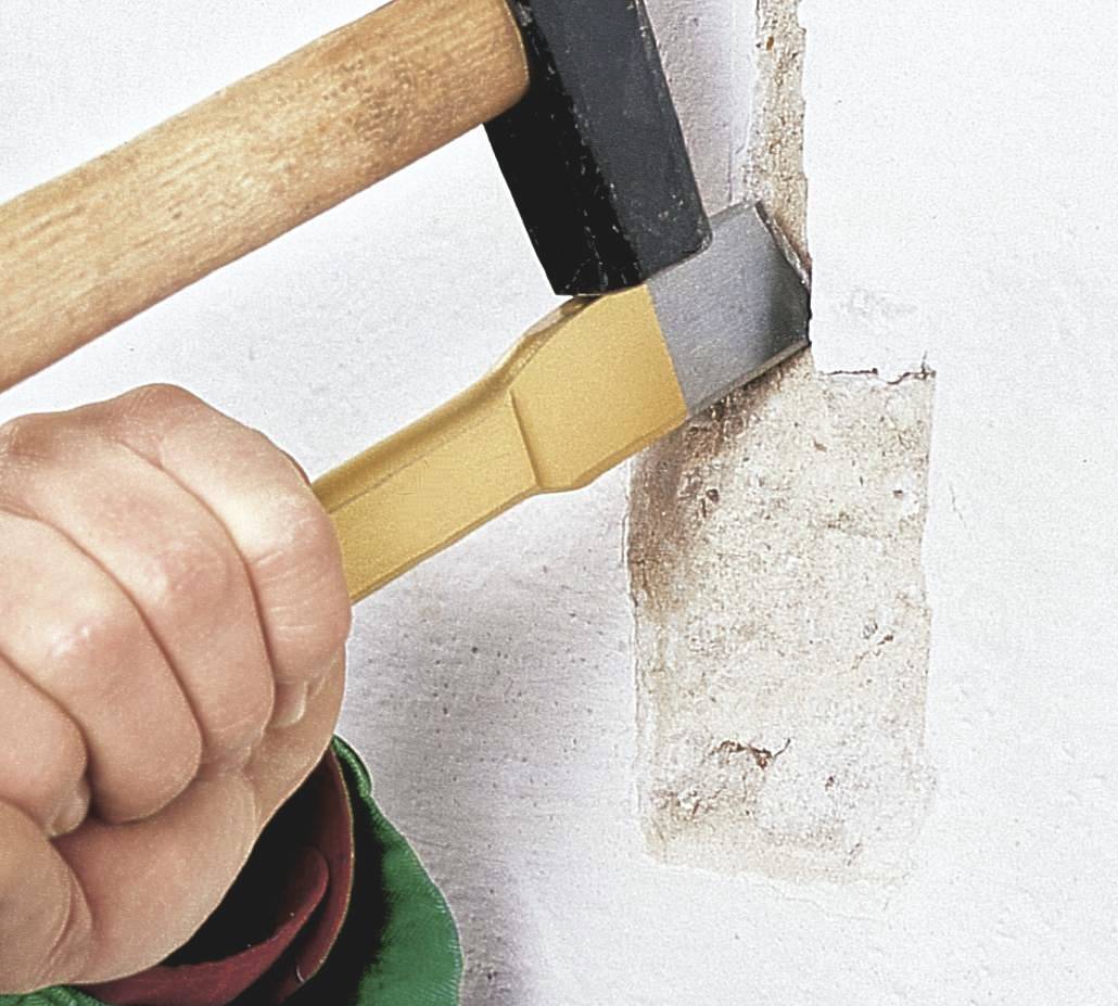 A person is using a hammer and chisel to remove plaster from a wall.