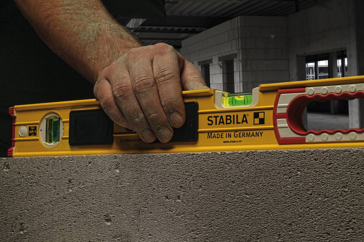 A hand is holding a yellow spirit level on a concrete surface. The spirit level indicates whether the surface is level.