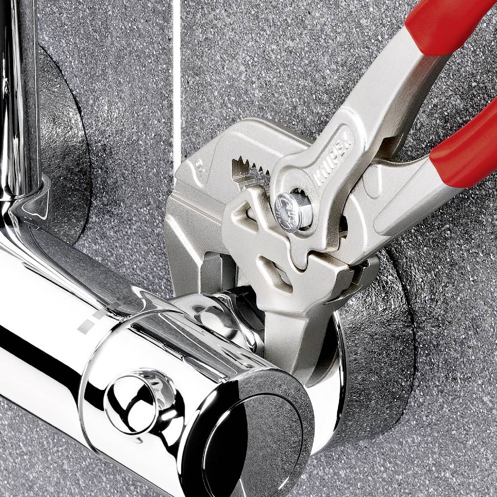 A pipe wrench tightens a chrome-plated fitting against a grey wall.