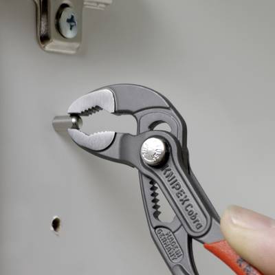 A hand is holding a water pump pliers that is tightening a screw on a metal part. The pliers are from the KNIPEX Cobra brand.