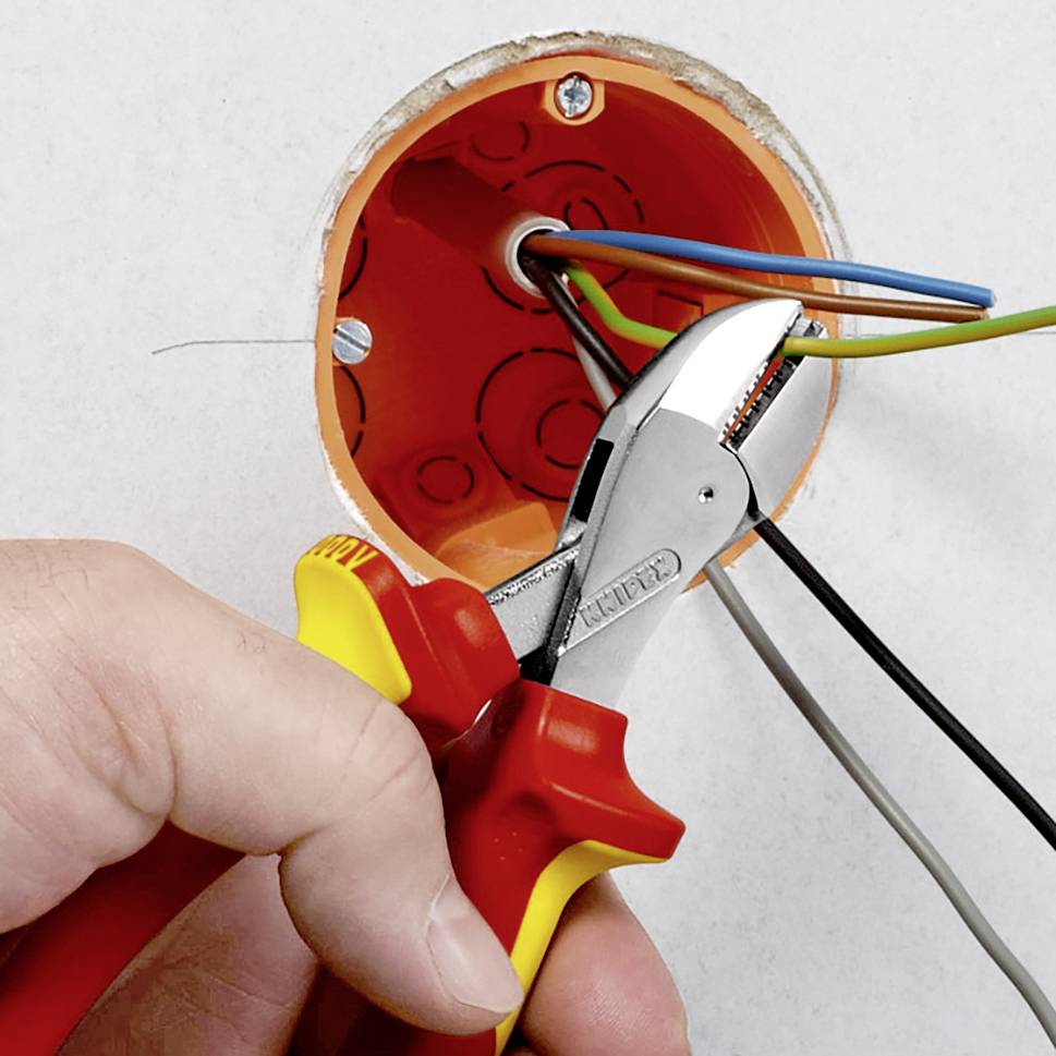 A hand is holding pliers to connect cables in an open cable socket. Electrical installation on wall mounting.