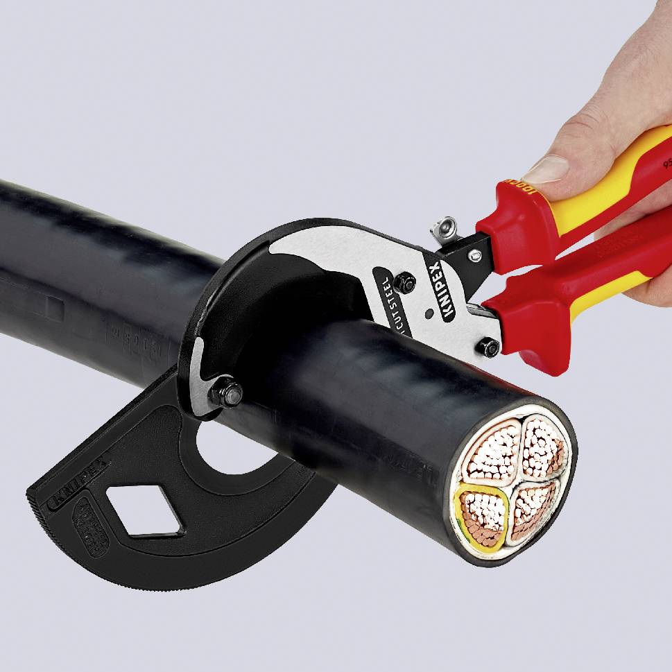 A hand holds a red pair of pliers cutting through a thick black cable, revealing the internal wires.