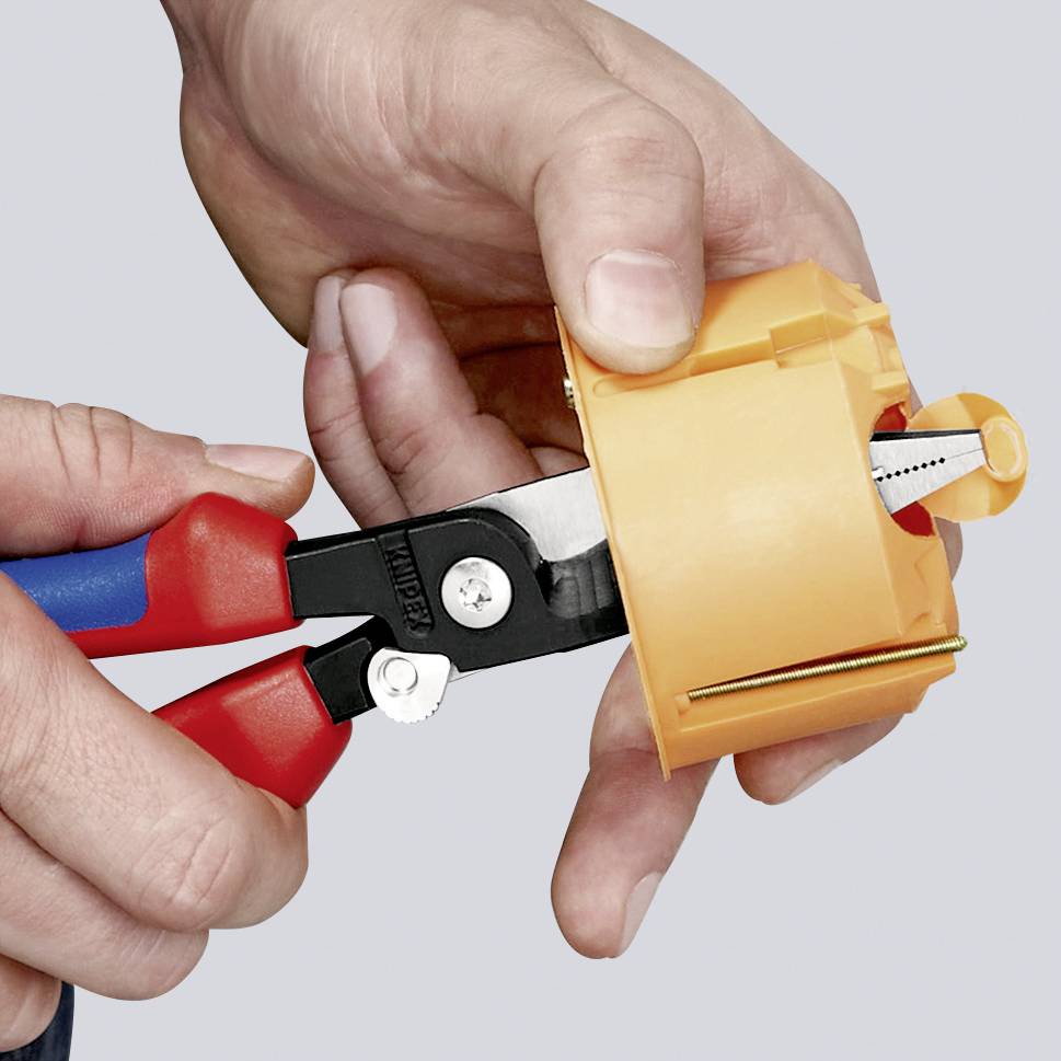 Two hands are holding a cable cutter to slice an orange cable. The pliers have red and blue handles.
