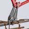 A red bolt cutter cuts reinforcement iron. Three steel rods are arranged in a metal frame.