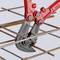 A red bolt cutter cuts through a reinforcing steel bar arranged in a lattice pattern.