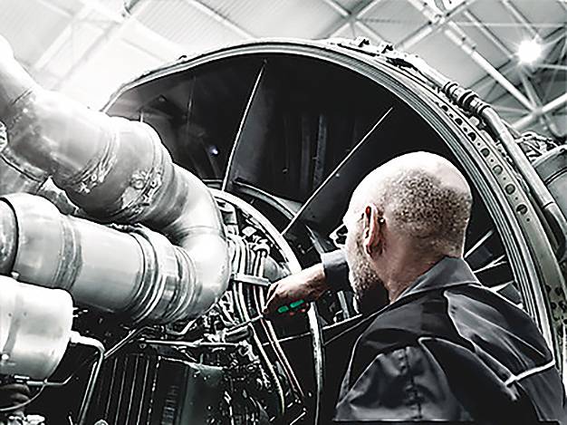 A person in a workshop inspects the intricate parts of a large engine, indicating technical maintenance or engineering work.