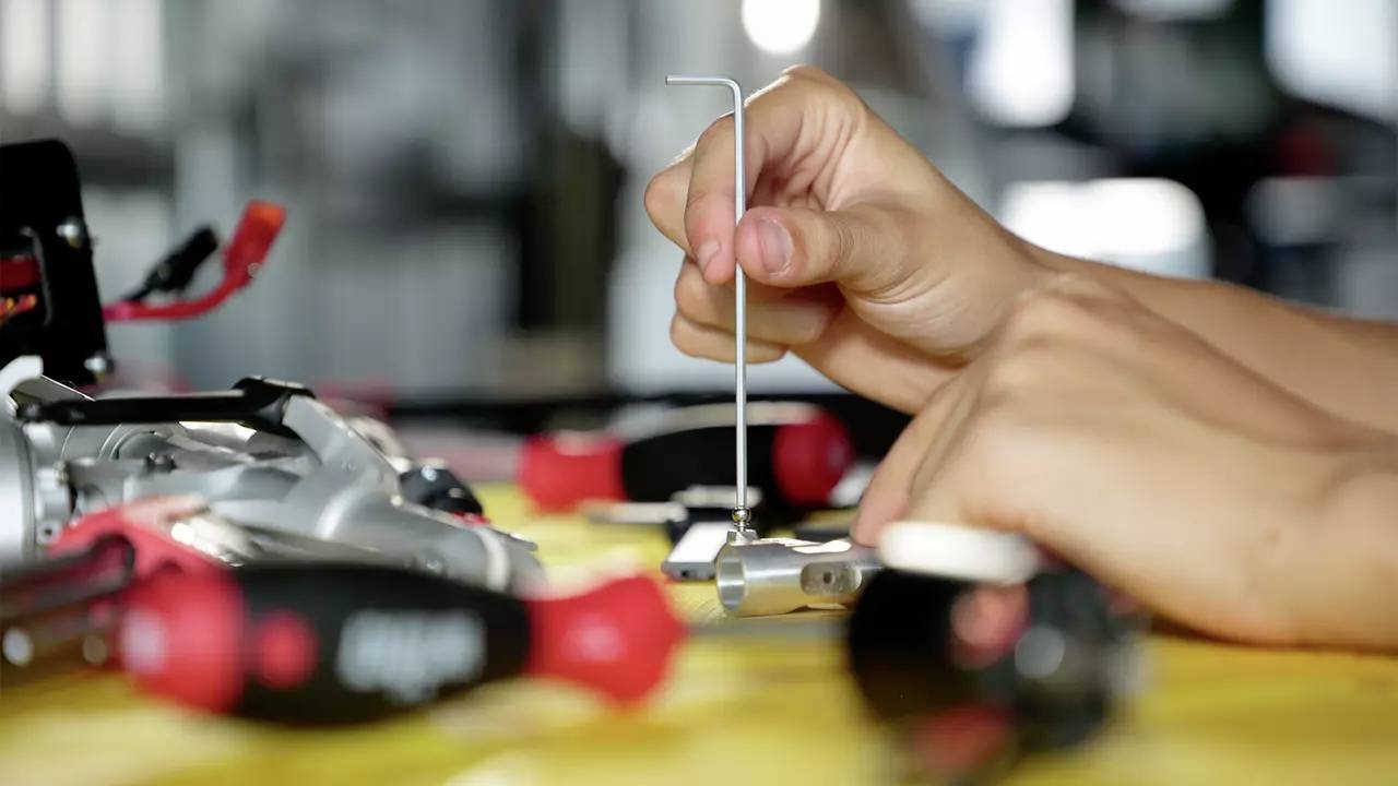 Two hands are working with an Allen key on a metal construction on a table with scattered tools in the foreground.