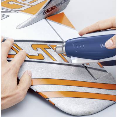 A person is holding a model aircraft and removing a sticker from the plane's wing using a blue hairdryer.