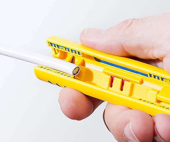 A hand is using a yellow cable stripper to remove insulation from a white cable.