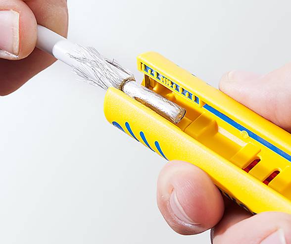 A close-up of hands using a yellow wire stripper tool to remove insulation from a wire, exposing inner metal strands.