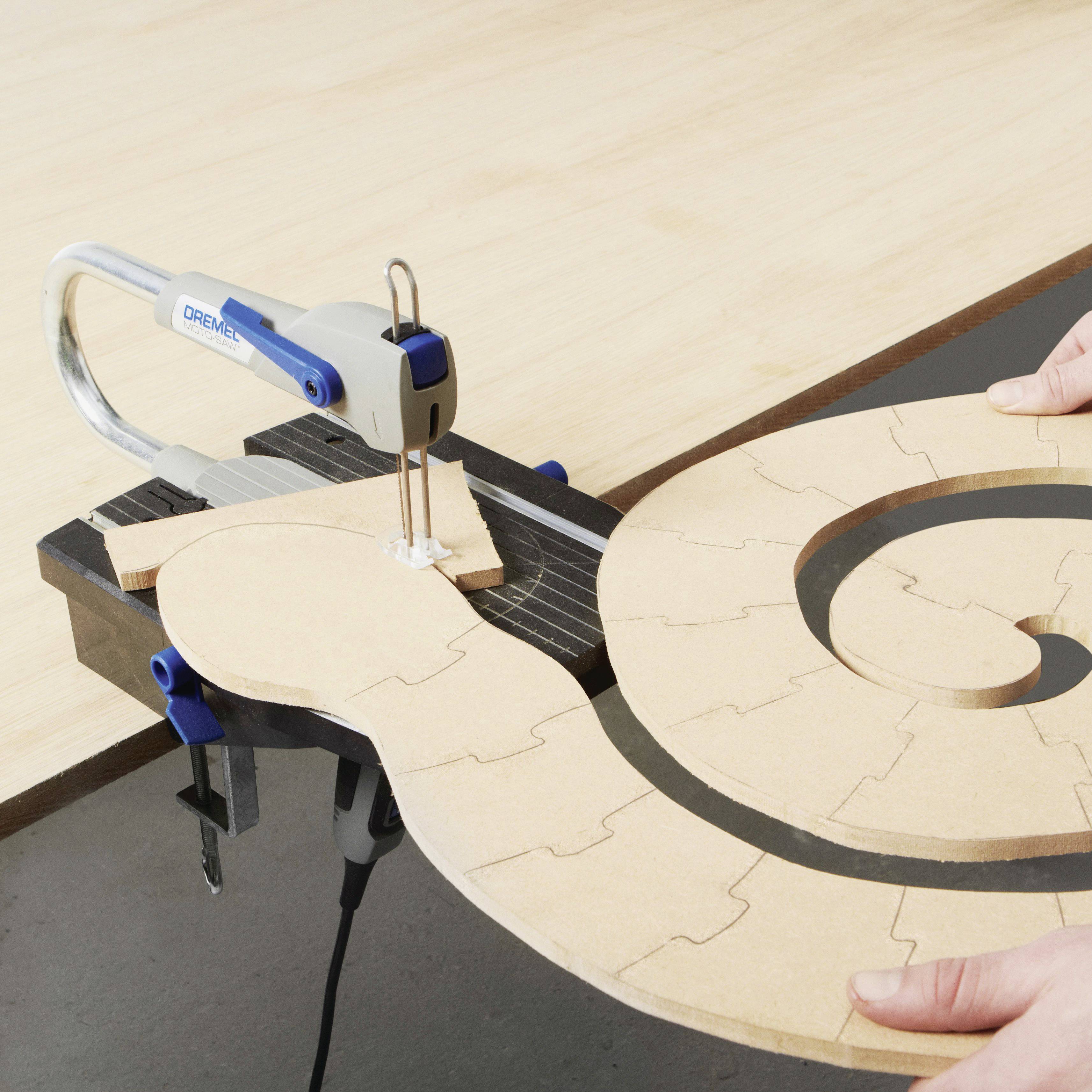 A jigsaw cuts a spiral-shaped form out of plywood. A person slowly guides the wood through the saw.