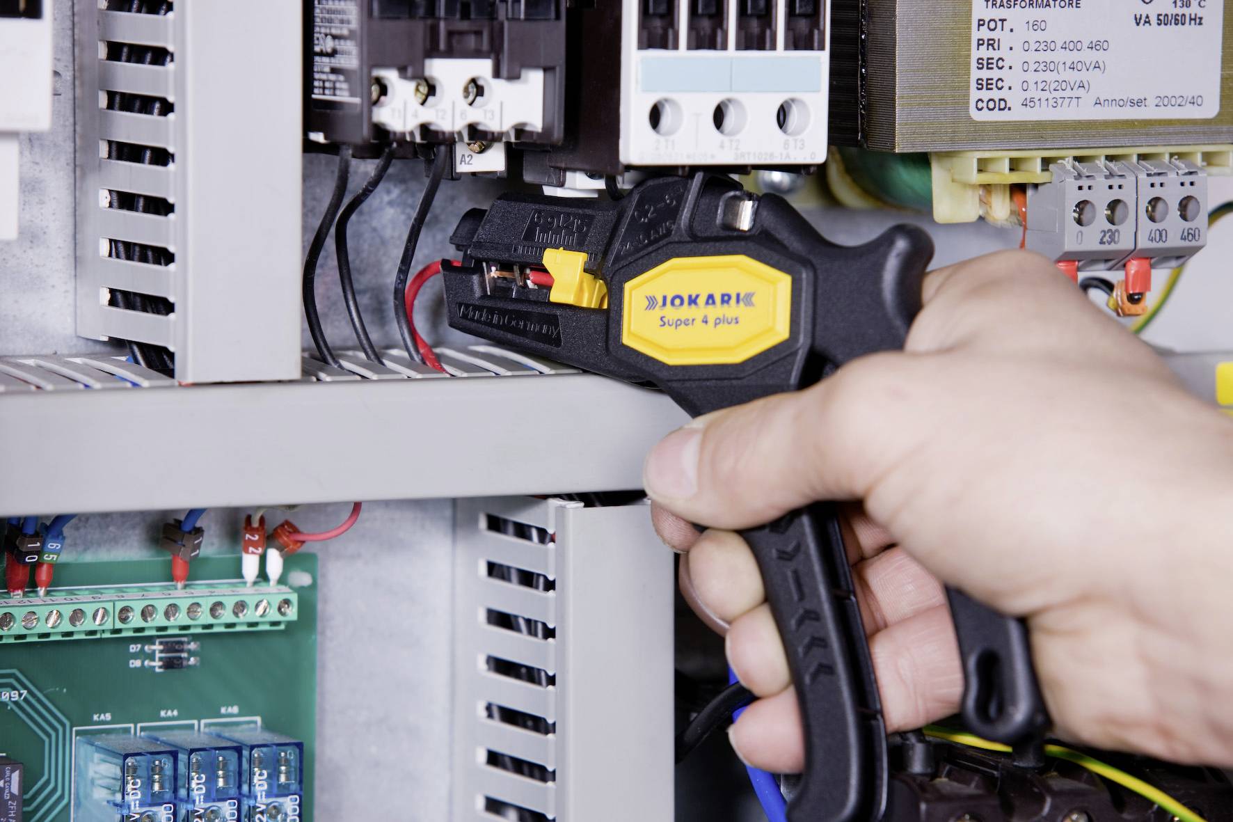 'Hand operating a cable stripper to process cables inside an electrical control cabinet.'