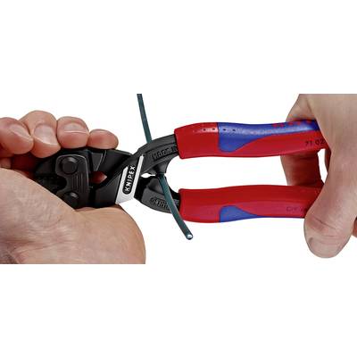 A person is using a red and blue Knipex cable cutter to cut through a green-sheathed cable.