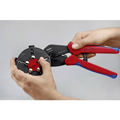 A person is holding a crimping tool with red handles, pointing it towards a round, black component with multiple openings.