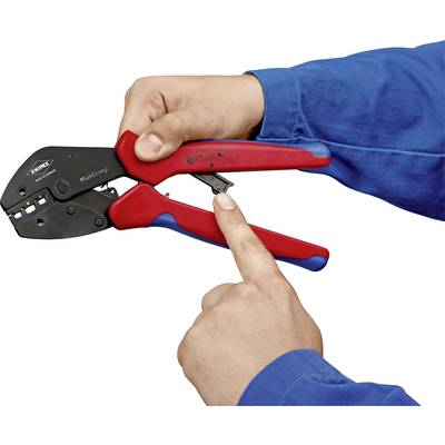 Two hands are holding a red and black crimping tool. One hand is pointing to a lever on the pliers. The person is wearing a blue jumper.