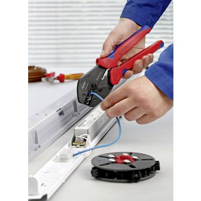 A person is using a crimping tool to connect an electrical connection on an LED light on a workbench.