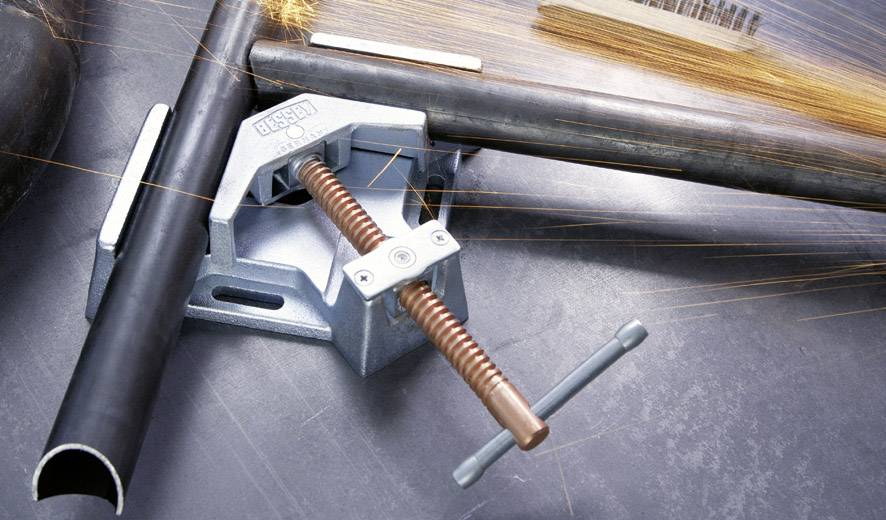 A pipe is held in a G-clamp while sparks are flying. A wire brush can be seen in the background.