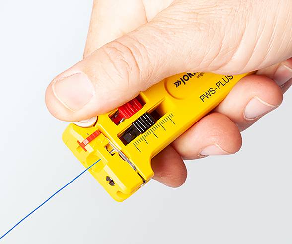 A hand holding a yellow wire stripping tool, partially stripping blue wire, with measurement markings on the tool's surface.