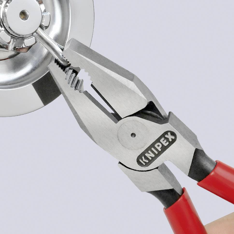 A pair of pliers is holding a metal nut in a pipe connection. The pliers have red handles and are pointing towards a chrome-plated connecting element.