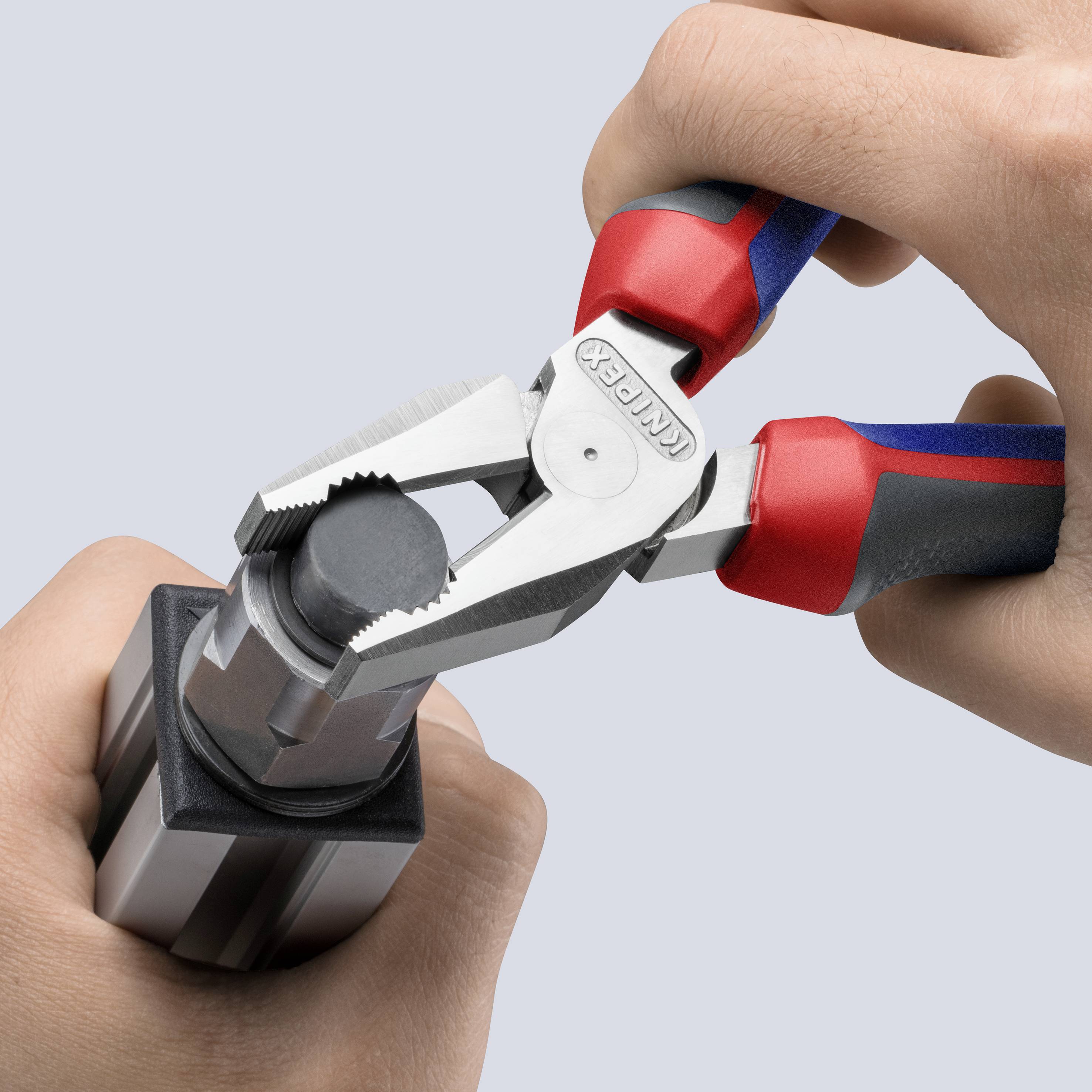 Two hands are holding a pair of pliers gripping a round object. The pliers have red and blue handles, and the object is black.
